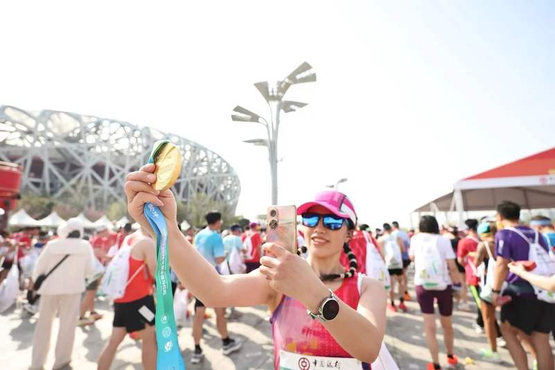 完赛选手拿着奖牌在鸟巢前拍照留念。