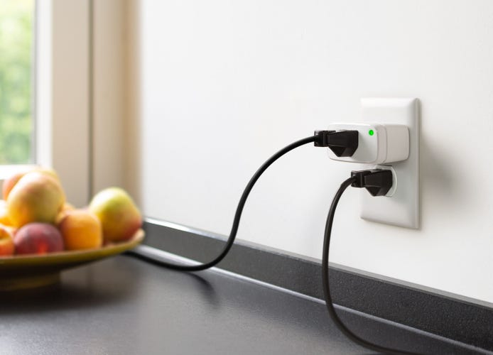 The Matter-compatible Eve Energy smart plug in the top socket of a kitchen outlet, with another cord plugged into the outlet below.