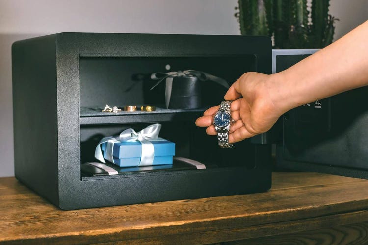 A hand reaches to put a watch in Yale safe already filled with belongings.