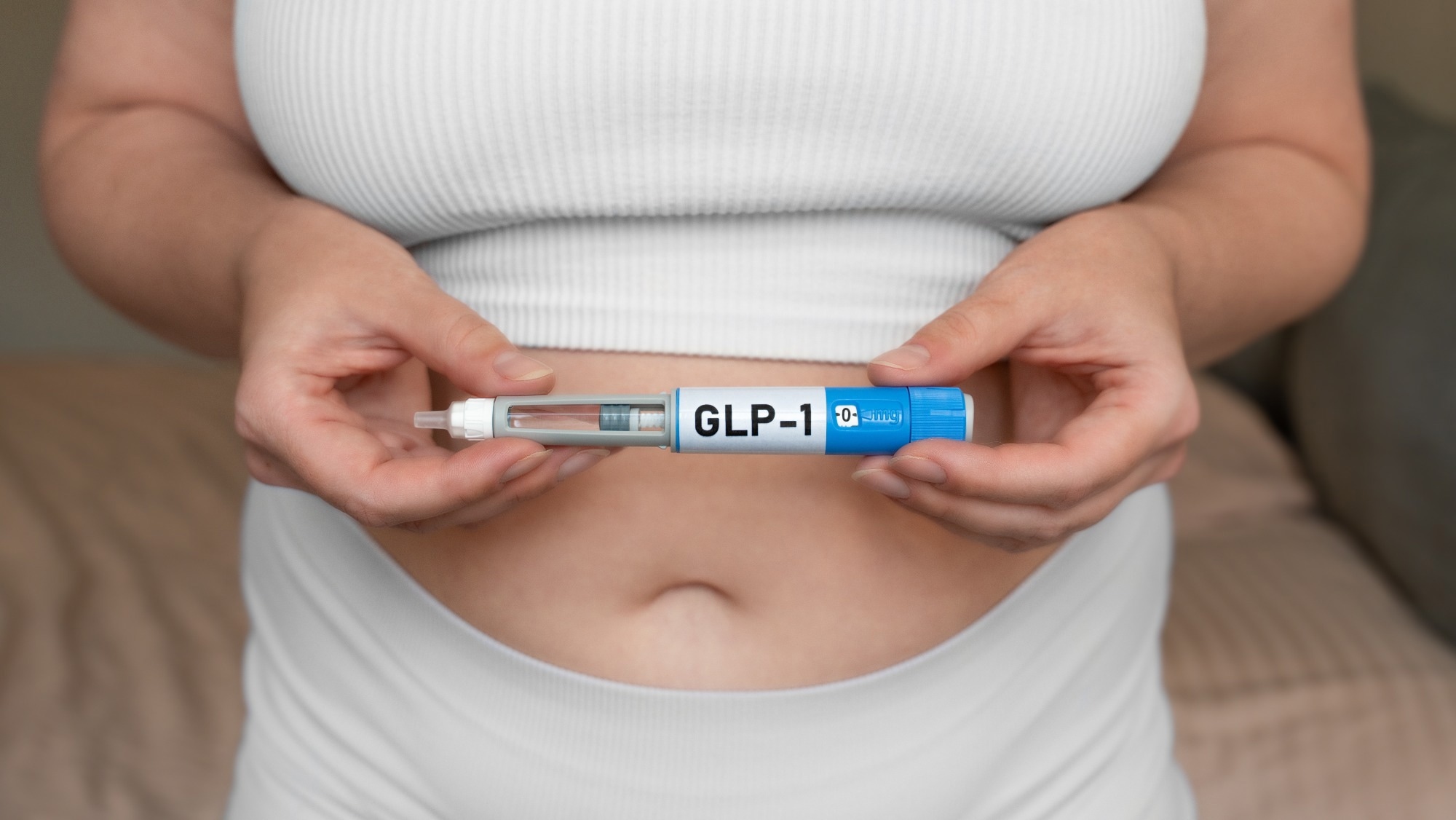 Close-up of woman holding GLP-1 injection pen near stomach, modern medical treatment for weight loss and blood sugar control
