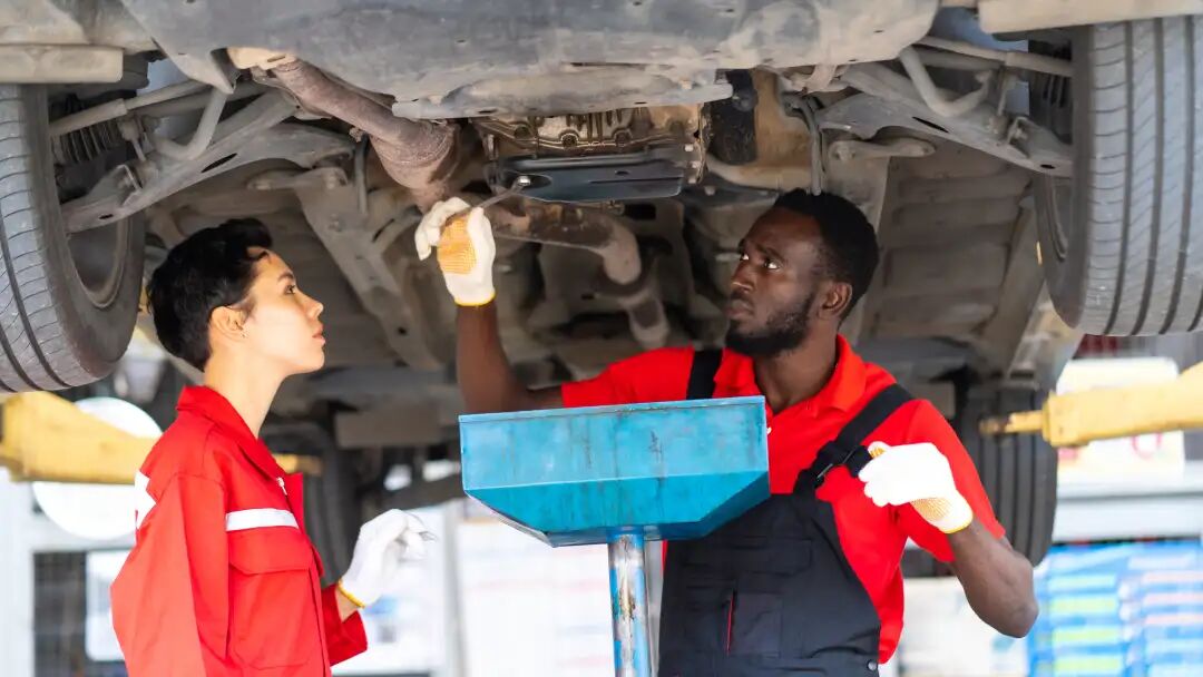 Black Male And Female trainee Mechanics Working Underneath Car Together Car maintenance and auto service garage.